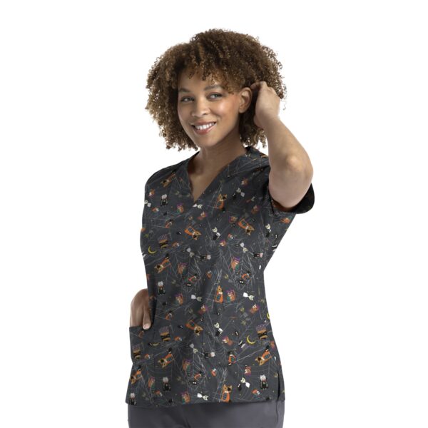 A printed curved V-neck top in dark fabric featuring a fun pattern with various motifs. The model has curly hair and a slight smile.