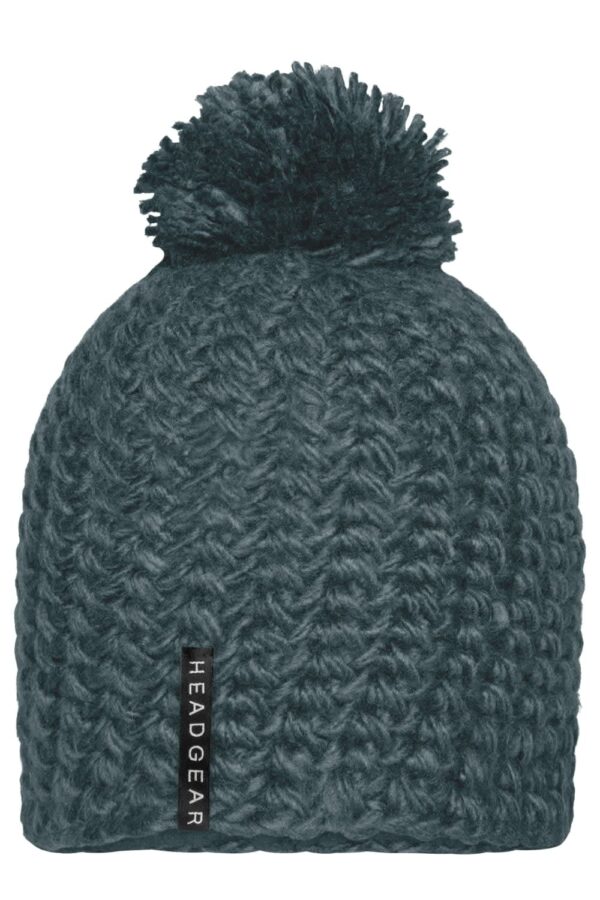 A unicoloured teal crocheted cap with a textured pattern and a fluffy pompon on top, featuring a small logo.