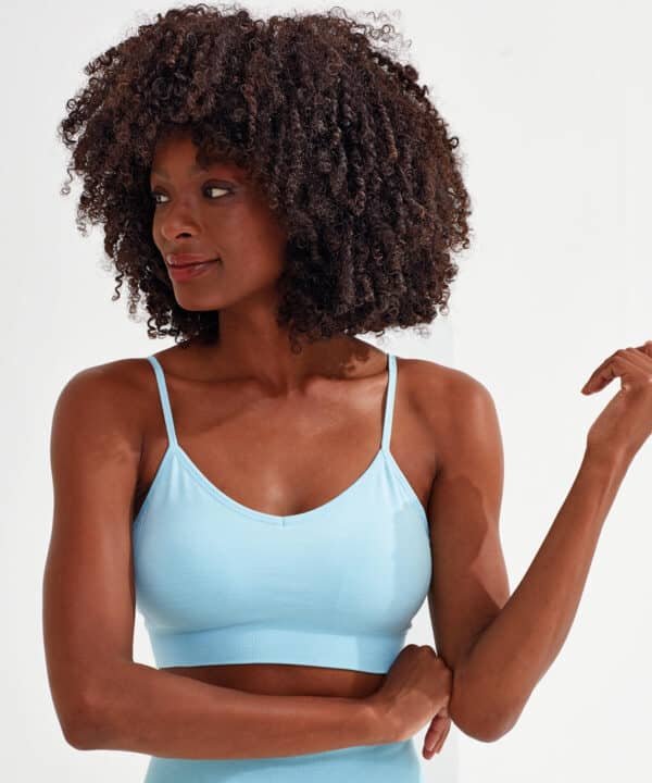 A light blue sport bra with seamless design and thin straps, featured on a model with curly hair and a neutral background.