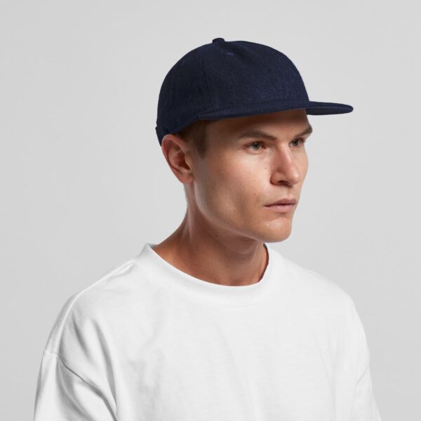 A navy wool cap with a flat brim, worn by a model in a white shirt. The cap features a logo.