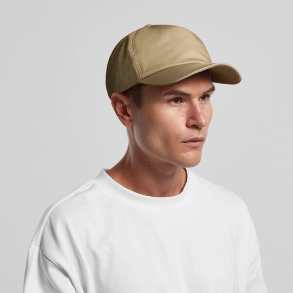 A beige cap is worn by a man with short hair, featuring a curved brim and a logo on the front.