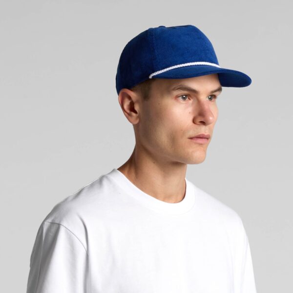 A blue cap with a curved brim and a decorative band, featuring a logo on the front, worn by a model.