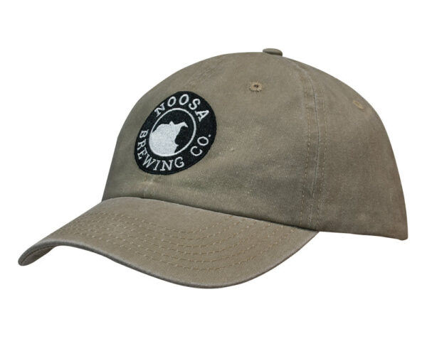 A beige cap made from enzyme washed, pigment dyed cotton twill, featuring a circular logo on the front.