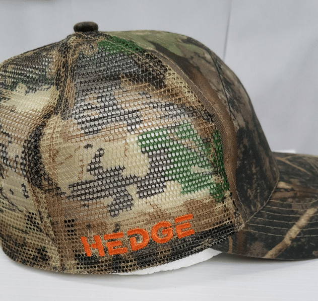 Orange logo embroidered on the mesh side panel of a camo trucker cap